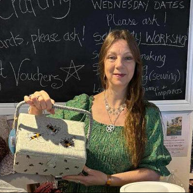 Woman holding a craft item in front of a chalkboard with text and fabric rolls in the background